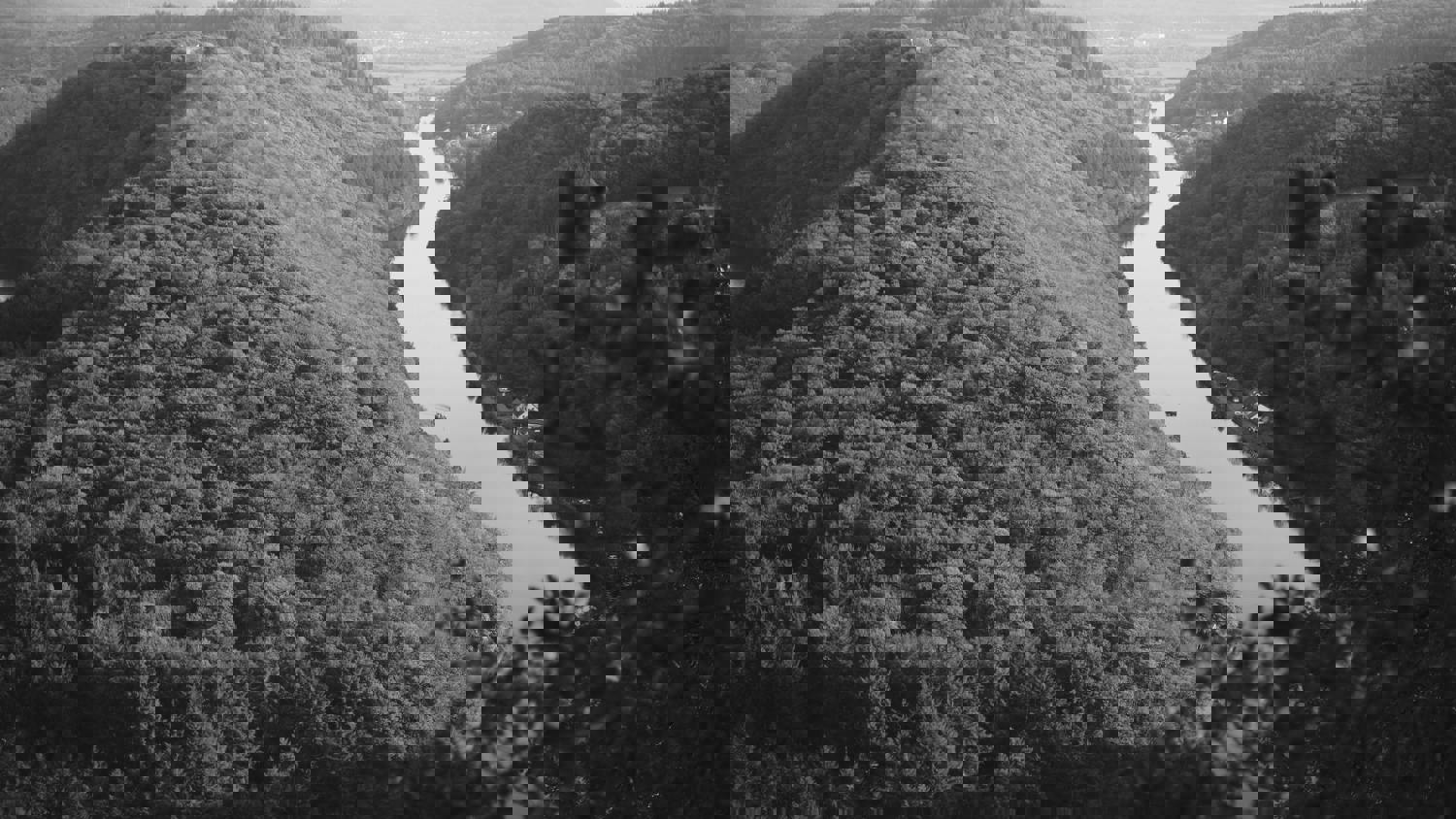 A distorted, pixelated black and white image of a river winding between forested hills, with digital glitches obscuring parts of the scenery.