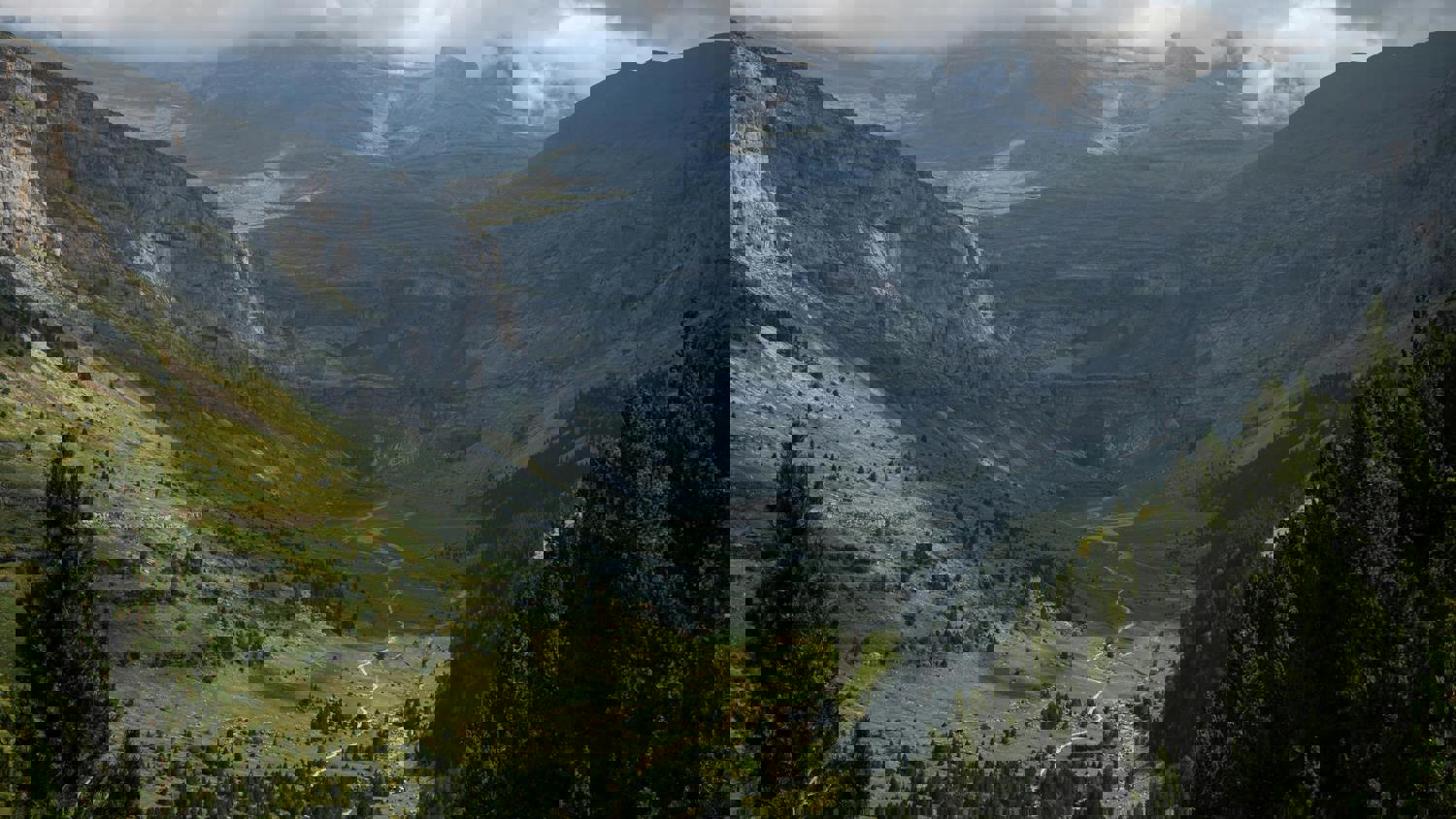A distorted, pixelated image of a mountain landscape with green valleys, rocky peaks, and cloudy skies, showing digital glitches throughout the scene.