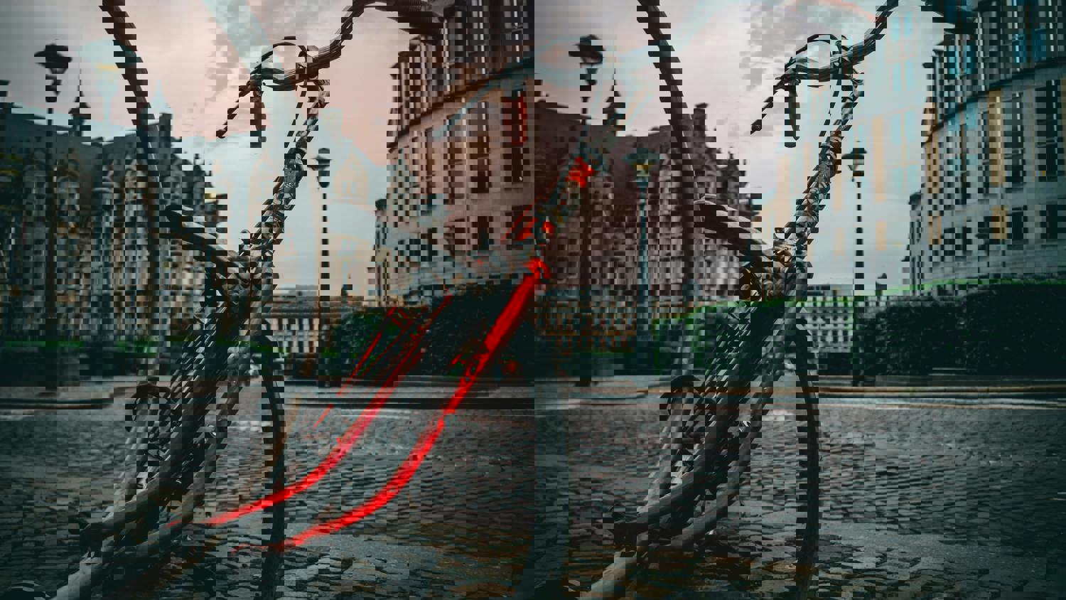 A city street with historic buildings is heavily distorted by digital glitches, with streaks of red and pixelated sections disrupting the image. Cobblestone pavement and greenery are visible among the visual noise.