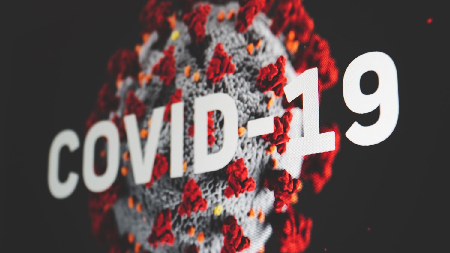 Illustration of a coronavirus particle with spike proteins against a black background. The word "COVID-19" is prominently displayed in bold white letters beside the virus.