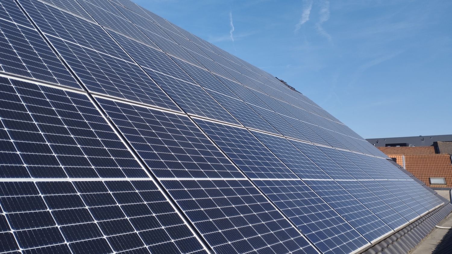 A close-up view of large solar panels installed on a rooftop with a clear blue sky and rooftops of nearby buildings in the background.