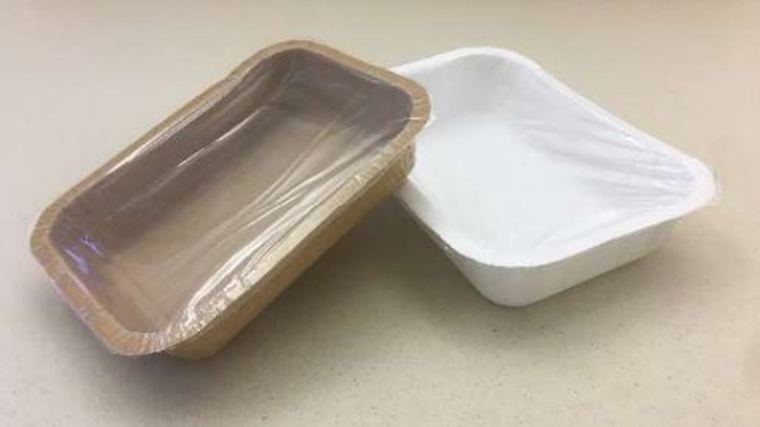 Two empty rectangular containers on a beige surface. The left container is brown with a clear plastic lid, and the right container is white with a partially visible clear plastic lid.