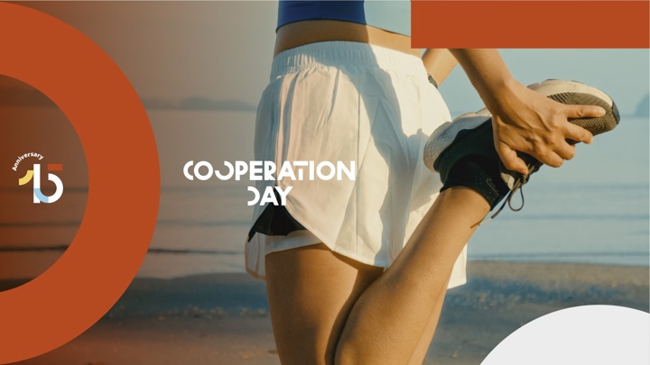 A person in athletic wear stretches their leg on a beach. The text "Cooperation Day" and a "15th Anniversary" logo are overlaid with orange and white geometric shapes.