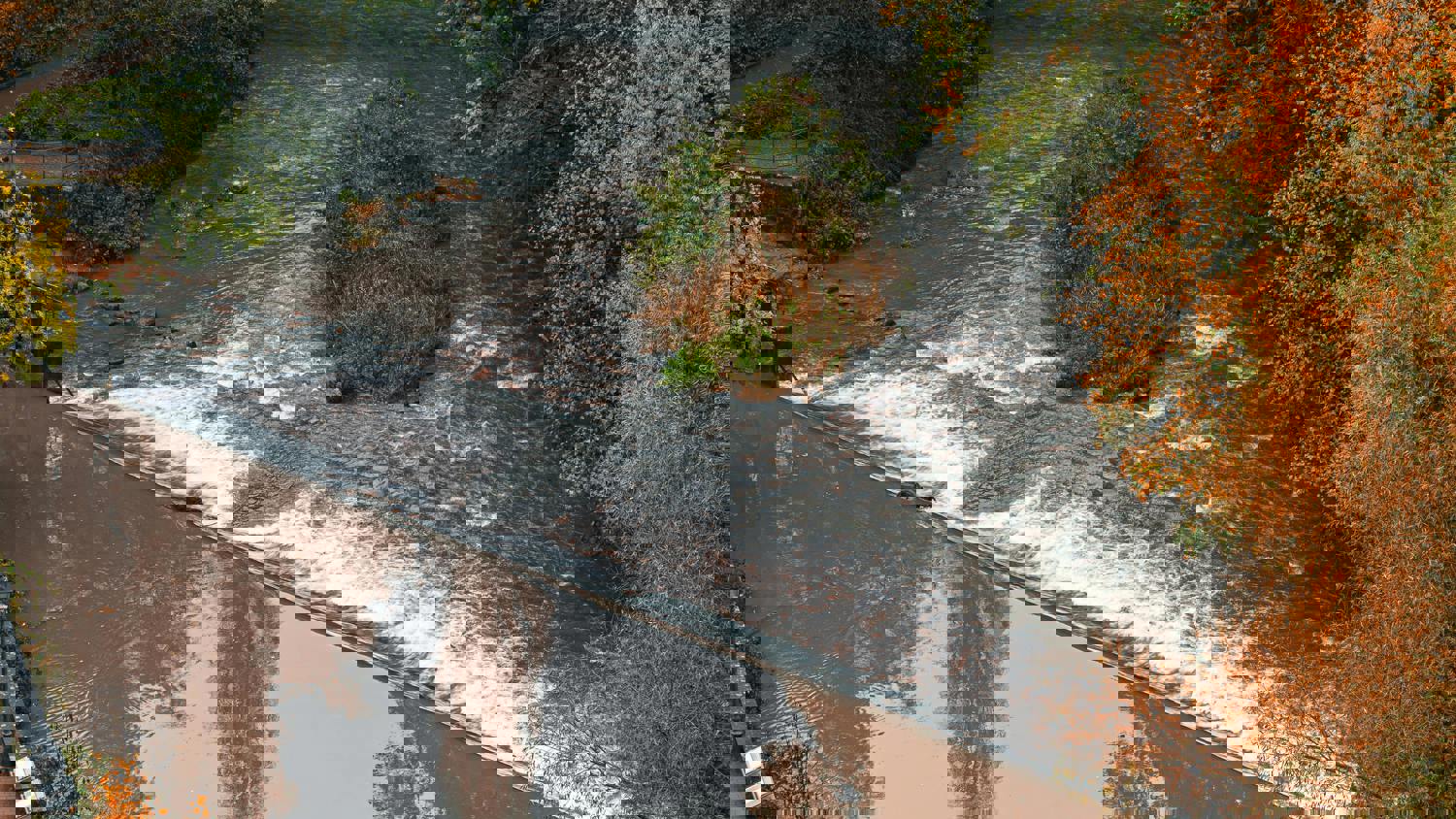 A river winds through a forest with autumn foliage, reflecting trees in the calm water. The image appears distorted, with visible digital glitches and color disruptions.
