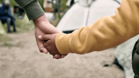 Two people holding hands at a campsite.