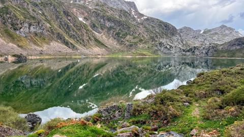 A glacial lake reflecting high, rocky mountain peaks under a cloudy sky.