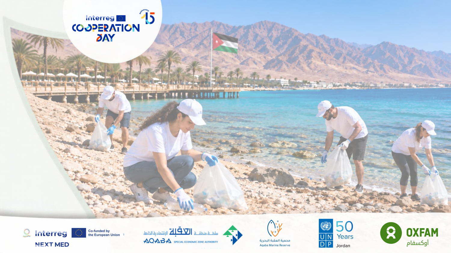Volunteers in white shirts and caps collect trash on a rocky beach by clear blue water, with palm trees and a Jordanian flag in the background. Various logos are shown at the bottom of the image.