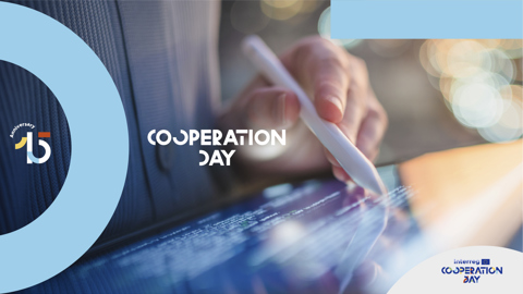 A person uses a stylus on a tablet with "Cooperation Day" text and anniversary logo, featuring blue accents and the Interreg logo in the bottom right corner.