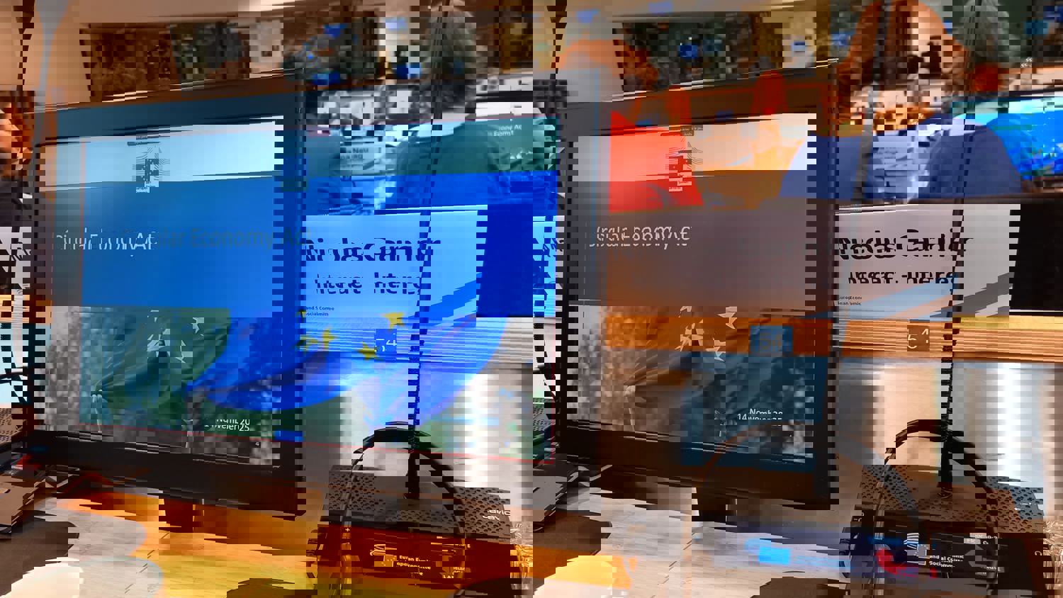 A group of people sit in front of large presentation screens in a modern conference room. The screens display text and visuals related to a climate or environmental discussion.