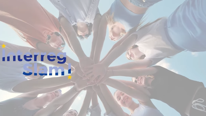 A group of people standing in a circle put their hands together in the center, viewed from below against a blue sky. The words "Interreg Slam!" with small yellow stars are overlaid on the left side.
