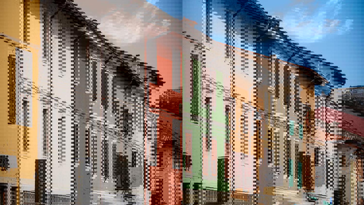 A fire escape with zigzagging metal stairs is attached to the side of a brick building, featuring railings and landings, seen from a low upward angle.