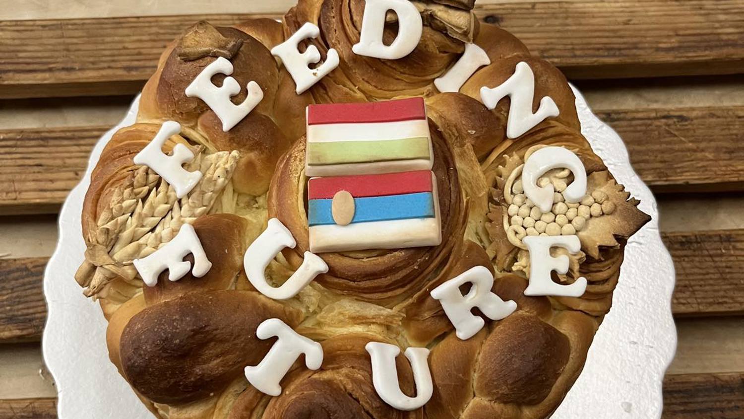A round loaf of bread decorated with the words "FEEDING FUTURE" in white letters and a small flag with blue, pink, and white stripes on top, displayed on a white board and wooden surface.