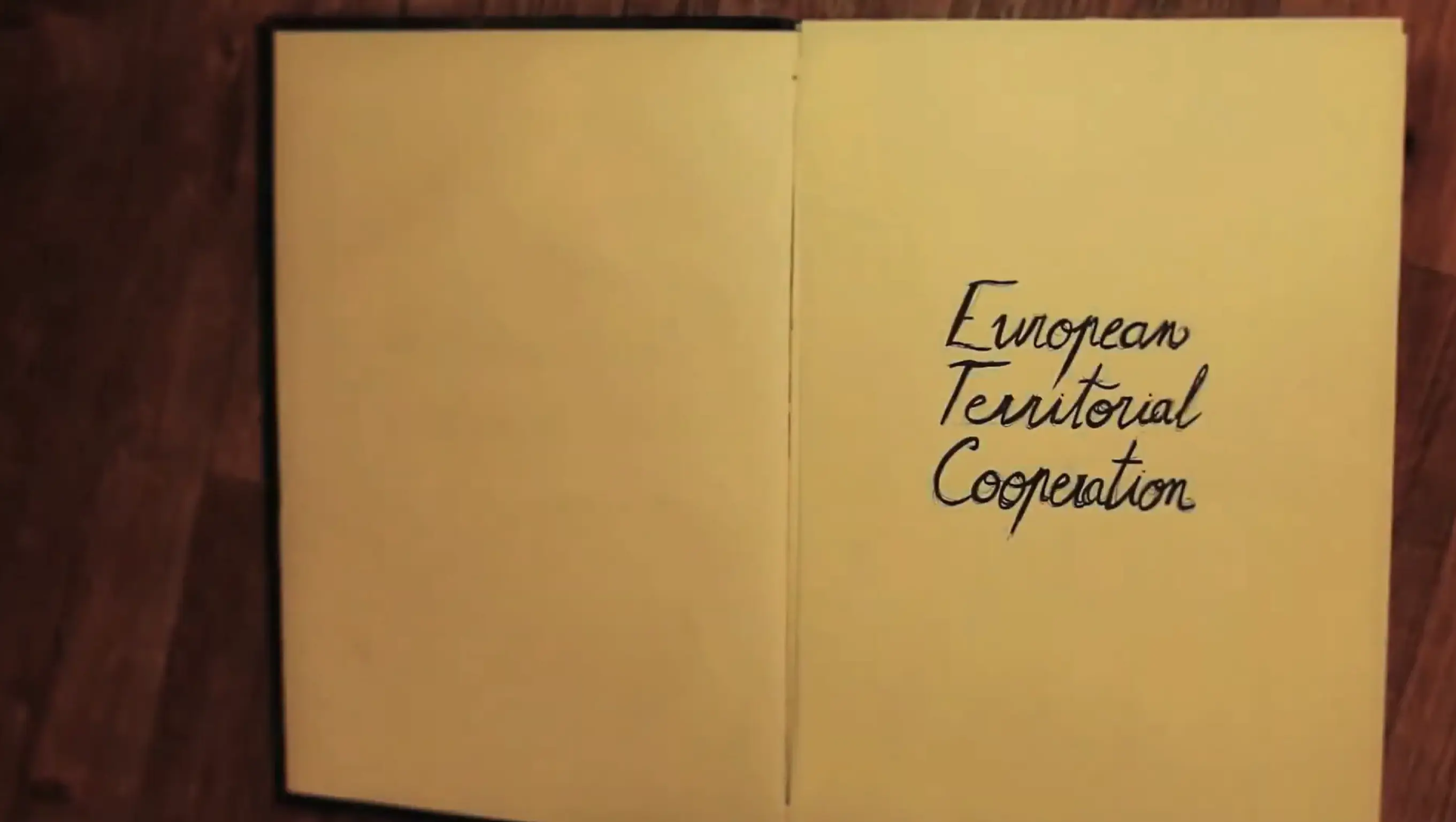 An open book lies on a wooden surface. On the right page, handwritten text reads "European Territorial Cooperation." The left page is blank.
