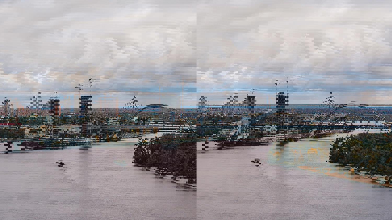 A city skyline with construction cranes and tall buildings is seen across a river, but the image appears digitally distorted with horizontal lines and glitches. The sky is mostly cloudy.